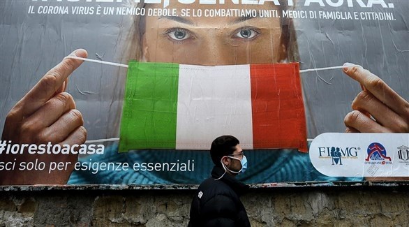إيطالي أمام لافتة تدعو لمكافحة كورونا بالكمامات (أرشيف)