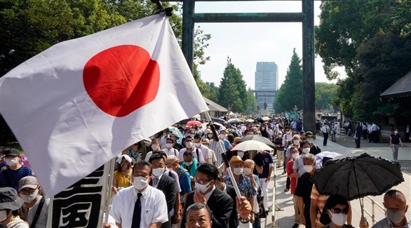 مجموعة من الأشخاص تمر بجانب بوابة توري حاملين العلم الياباني في طوكيو (اي بي ايه)