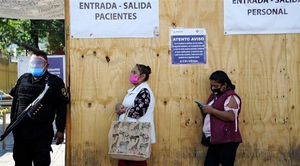 شرطي مكسيكي إلى جانب سيدتين أمام مركز فحص صحي في مكسيكو (أرشيف)