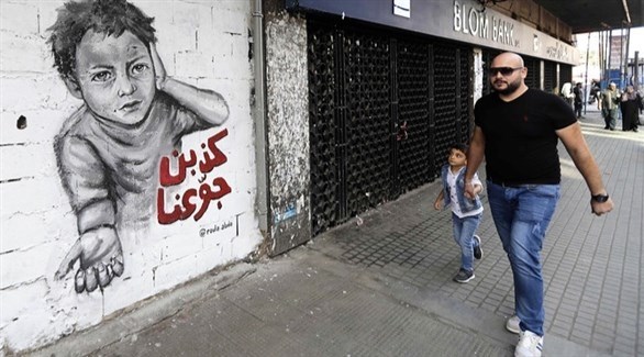 رجل يمسك طفلاً من يده في بيروت أمام جدارية تندد بالطبقة السياسية (أرشيف)
