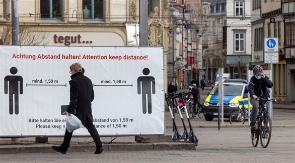 مواطنون ألمان بجوار لوحة إرشادية حول إجراءات وقاية كورونا (أرشيف)