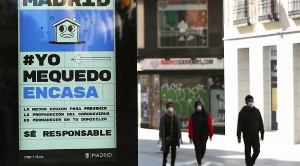 إٍسبانن في مدريد أمام لافتة تدعو للبقاء في البيوت (رويترز)