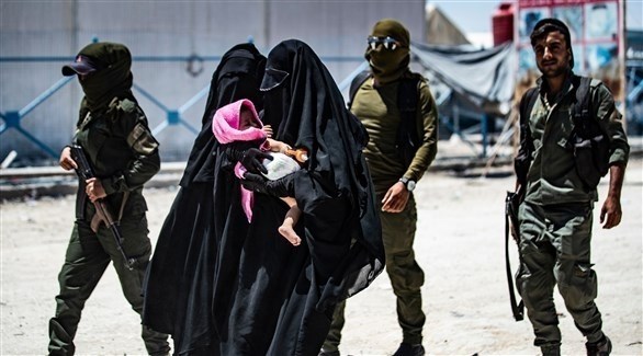 سيدة تحمل طفلها قرب مسلحين شمال سوريا (أ ف ب)