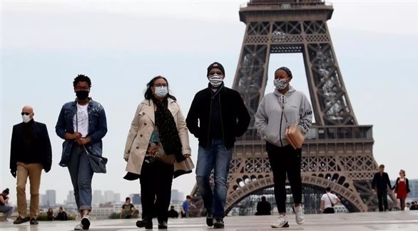 أشخاص يرتدون كمامات أمام برج إيفل بالعاصمة الفرنسية باريس (أرشيف)