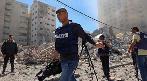 صحافيون بجانب مبنى تعرض للتدمير في غزة (أ ف ب)