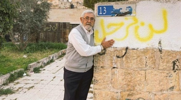 فلسطيني من حي الشيخ جراح يقف إلى جانب عبارة لن نرحل المكتوبة على جدار منزله (أرشيف)