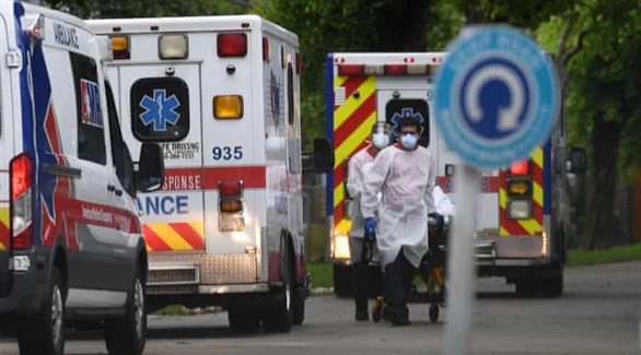 مسعفان أمام طابور من سيارات الإسعاف ينقلان مصاباً بكورونا إلى مستشفى في فلوريدا (أرشيف)