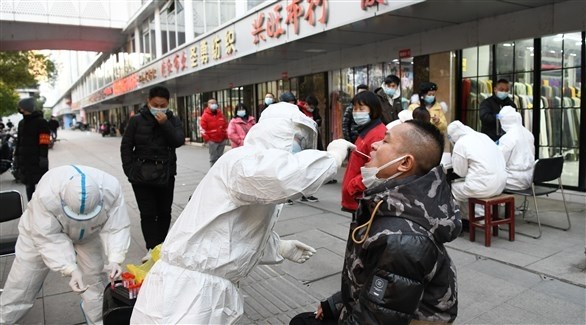 عاملون طبيون يفحصون صينيين في شارع لكشف الإصابات بكورونا (أرشيف)