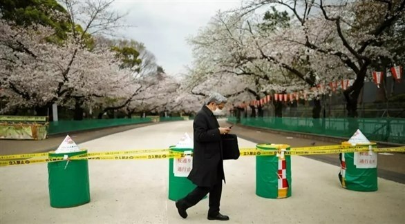 شخص يرتدي كمامة يمر بجانب حديقة مغلقة في طوكيو (أرشيف)