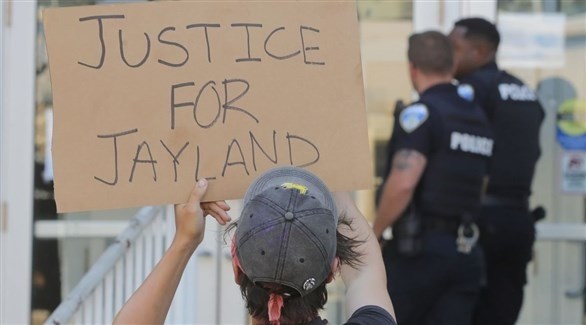أمريكي يرفع لافتة تطالب بالعدالة لجايلاند أمام عناصر من الشرطة (تويتر)