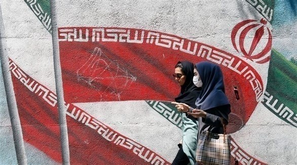 إيرانيتان تمران بجانب جدارية بالعلم الإيراني (شترستوك)