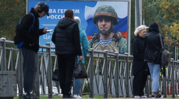روس في سان بطرسبوغ أمام لافتة تدعو للتجنيد (رويترز)