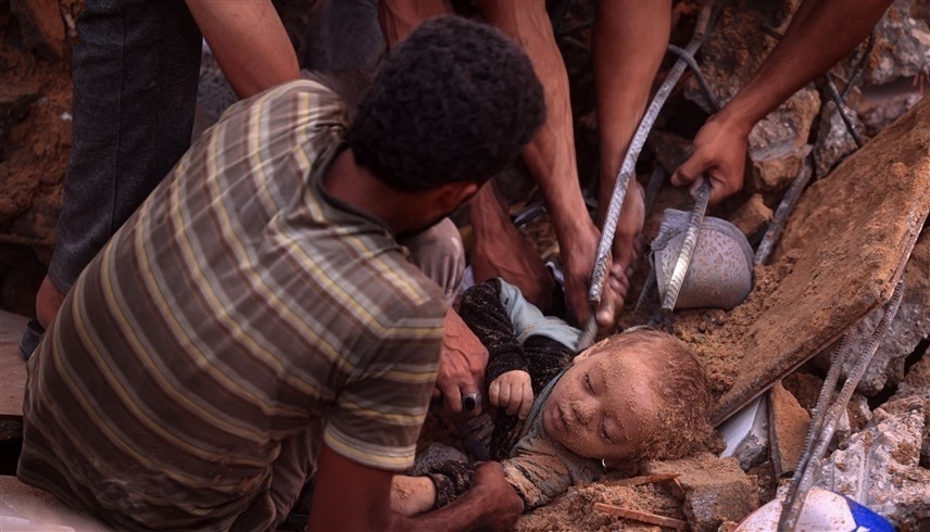 فلسطينيون يخرجون طفلاً ميتاً من تحت الأنقاض في غزة (أ ف ب)