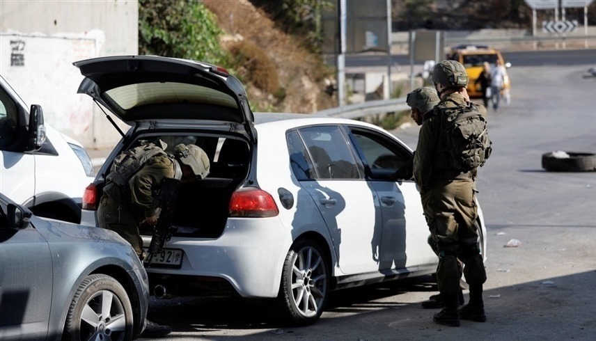 جنود إسرائيليون يقومون بتفتيش سيارة فلسطيني على حاجز في مدينة الخليل (رويترز)
