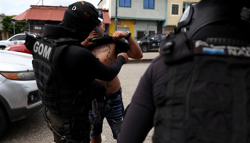 ضابط إكوادوري يتفقد شخصًا عند نقطة تفتيش وسط موجة العنف (رويترز)
