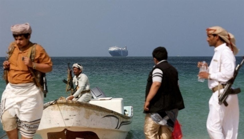 مسلحون يقفون على الشاطئ فيما ترسو السفينة  غالاكسي ليدر، التي استولى عليها الحوثيون (رويترز)